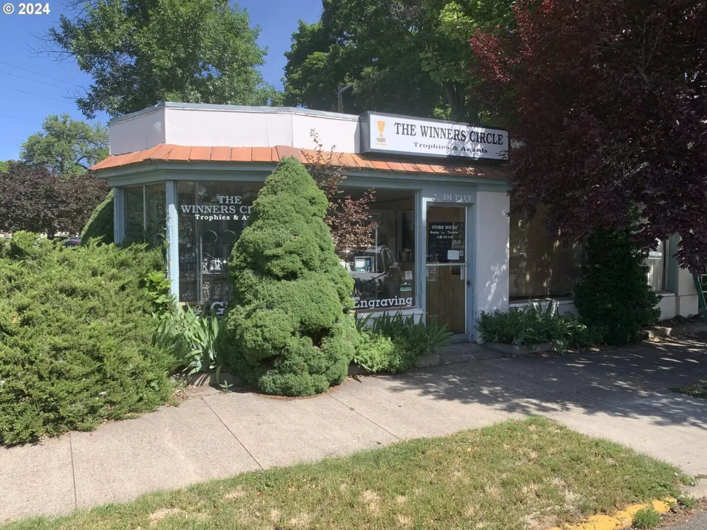 A small store with trees and bushes in front of it.