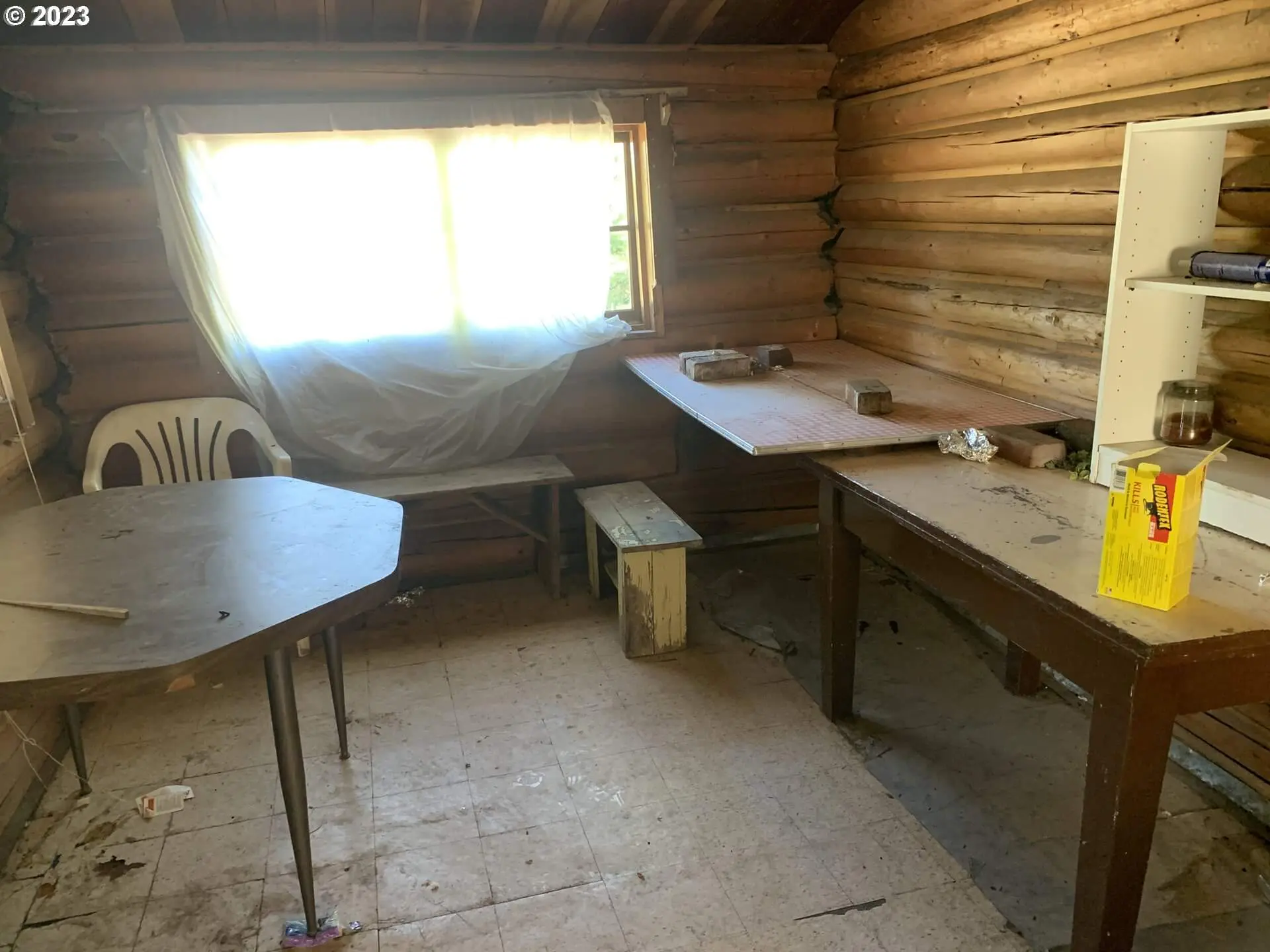 A room with wooden walls and floors, two tables and a chair.