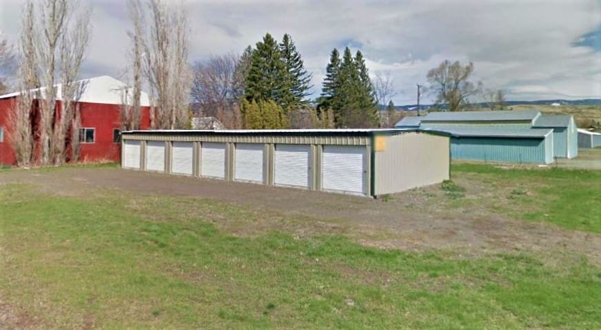 A row of garages in the grass near trees.