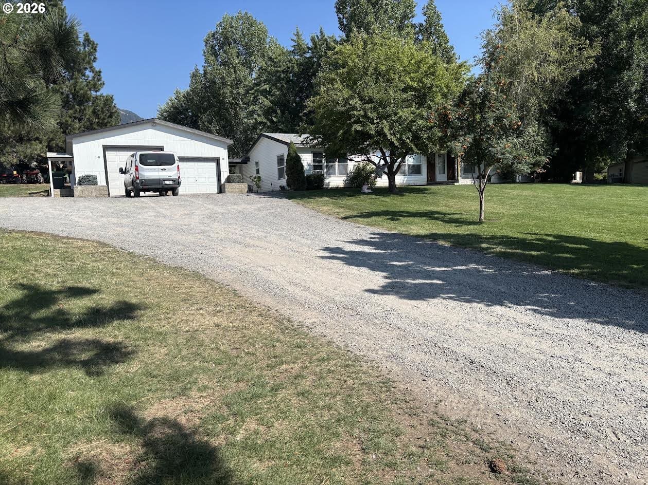 White house with gravel driveway and greenery.