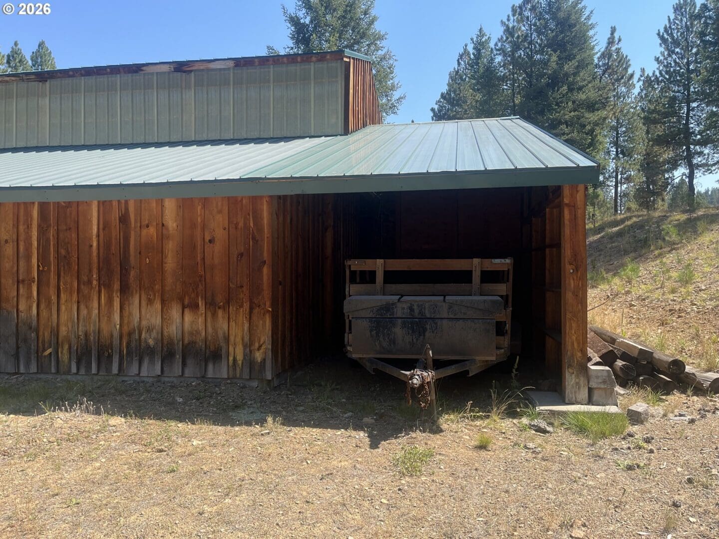 Wooden shed with trailer and surrounding trees.