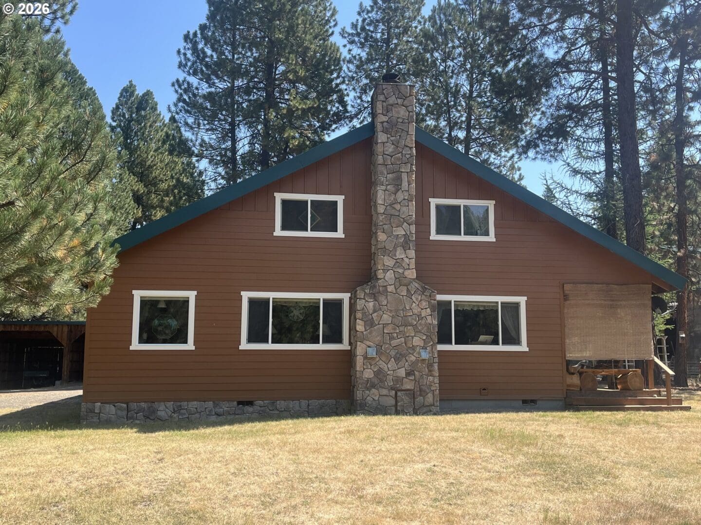 Brown house with stone chimney and trees.